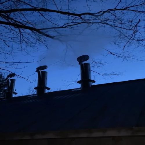 The sugarhouse at dusk, steam rising against the sunset